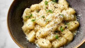 Creamy pesto gnocchi cooking in skillet with melted parmesan and fresh herbs