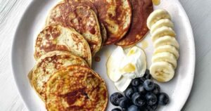 High protein banana pancakes stacked on white plate with banana slices and syrup drizzle