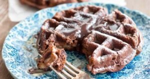 Keto brownie waffles served on white plate with sugar-free maple syrup and chocolate chips