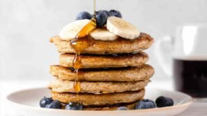 Protein oatmeal blender pancakes stacked high with fresh blueberries and maple syrup drizzle