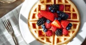 Fluffy protein waffles stacked with fresh berries and maple syrup drizzle