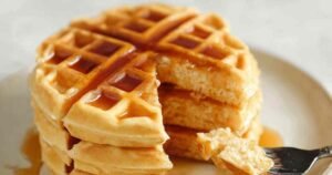 Protein powder waffles served on white plate with butter and sugar-free syrup drizzled on top