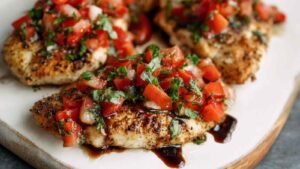 Bruschetta chicken topped with fresh tomatoes and herbs on white plate