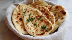 Cottage cheese garlic naan cooking in cast iron pan showing golden brown color