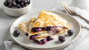 Blueberry Breakfast Quesadilla cut into wedges on white plate with fresh blueberries