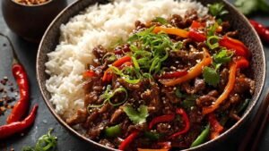 Crispy chilli beef rice in a white bowl with chopsticks and garnishes
