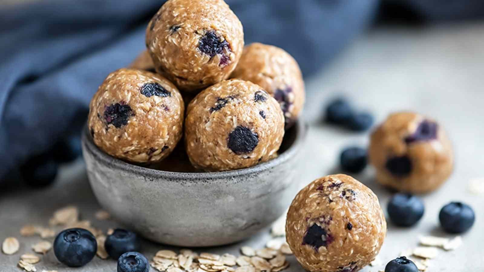 Homemade blueberry muffin protein balls arranged on white plate with scattered oats and